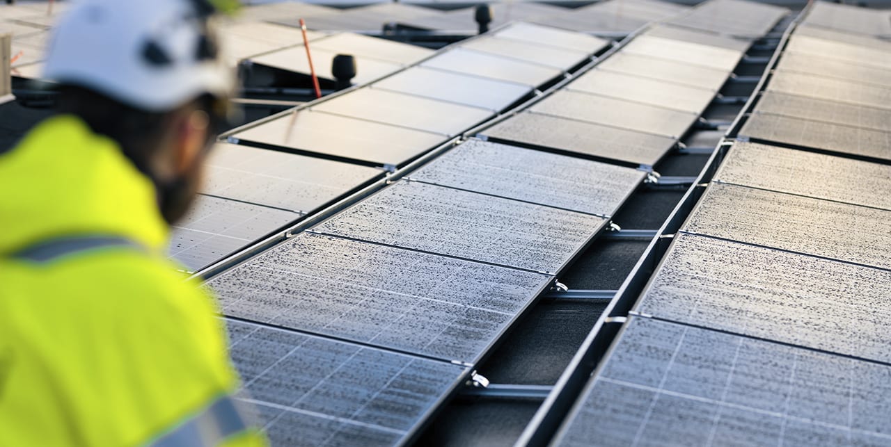 Työntekijä tarkistaa aurinkopaneeleja rakennuksen katolla.